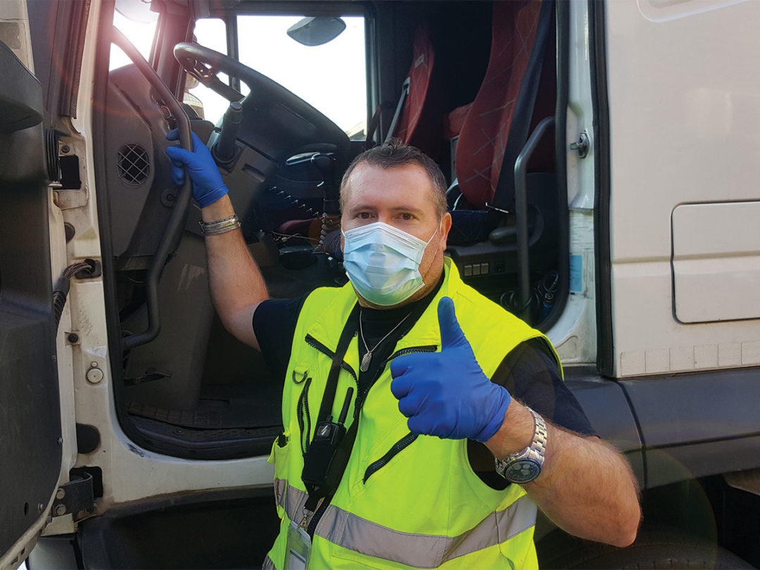 Truck driver wearing mask next to truck giving thumbs-up signal